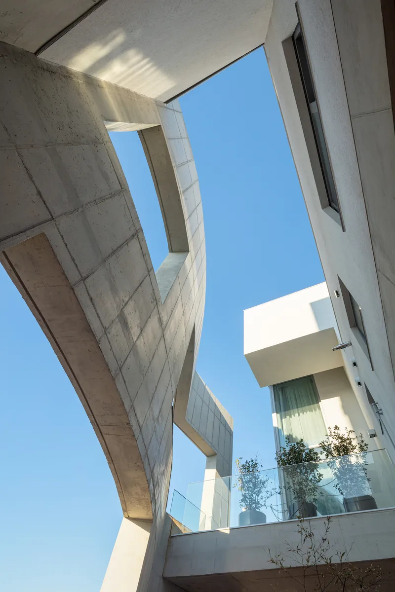 Upward view into a concrete courtyard with angled walls framing sky and balcony plantings