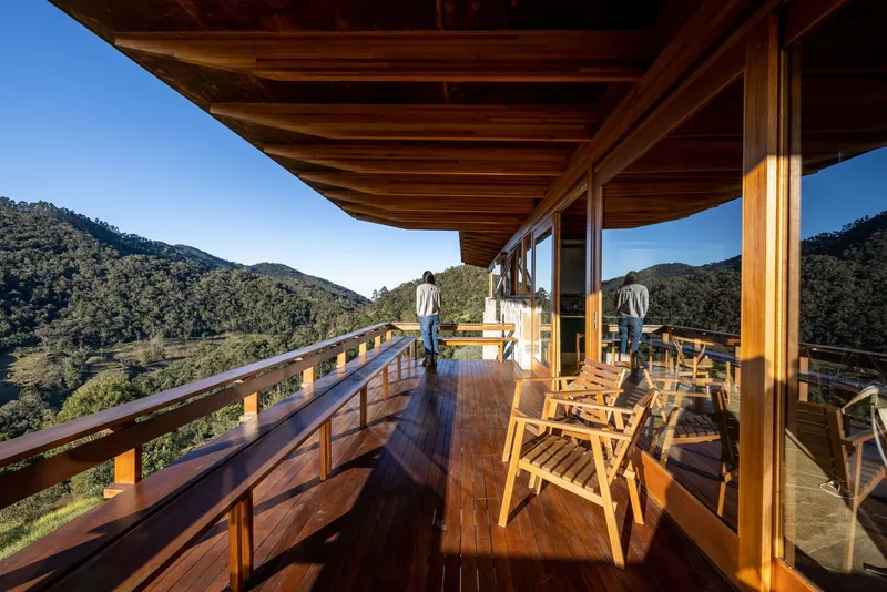 Covered deck with exposed timber rafters and railing where two figures look out over forested valley