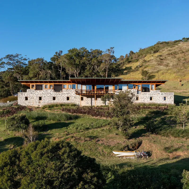 Stone masonry base with timber-framed upper level set into a grassy hillside under clear blue sky