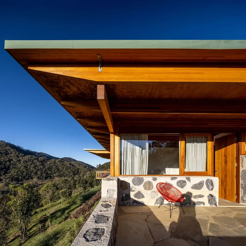 Covered terrace with exposed timber beams and river stone wall overlooking mountain slopes in afternoon light