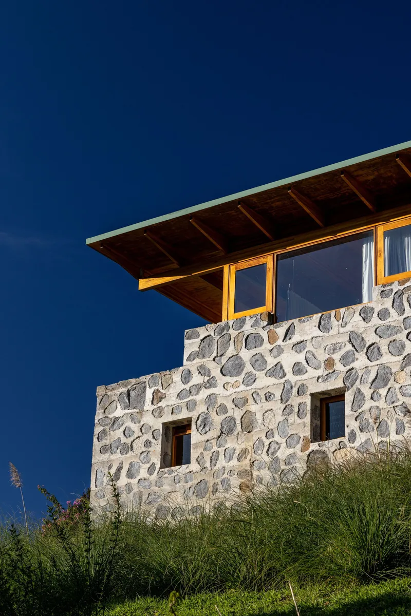 Upper level facade with river stone walls and timber roof overhang against deepening twilight sky