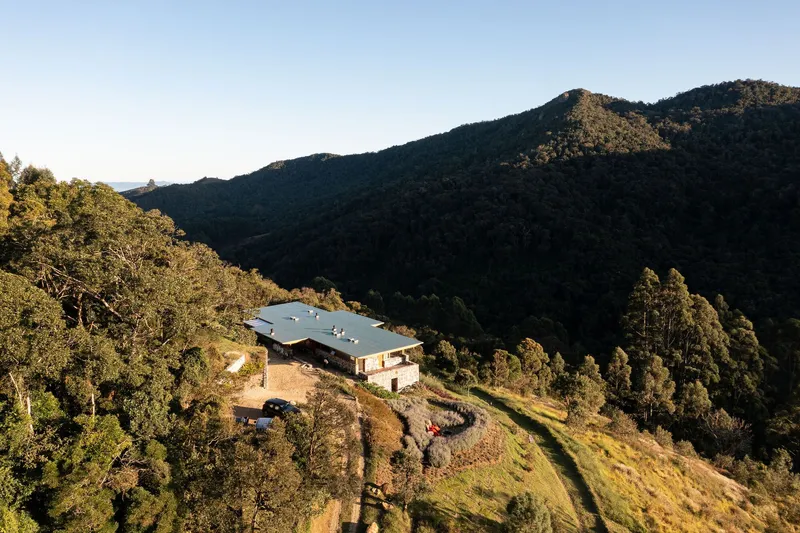 Aerial view of the three-lobed metal roof nestled into a forested mountainside in afternoon light
