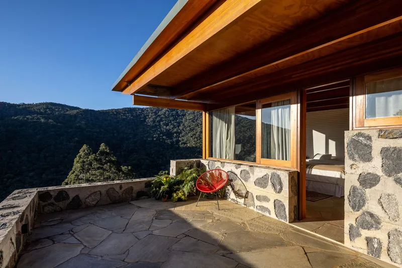Covered terrace with exposed timber beams, stone paving, and a red lounge chair facing mountain views