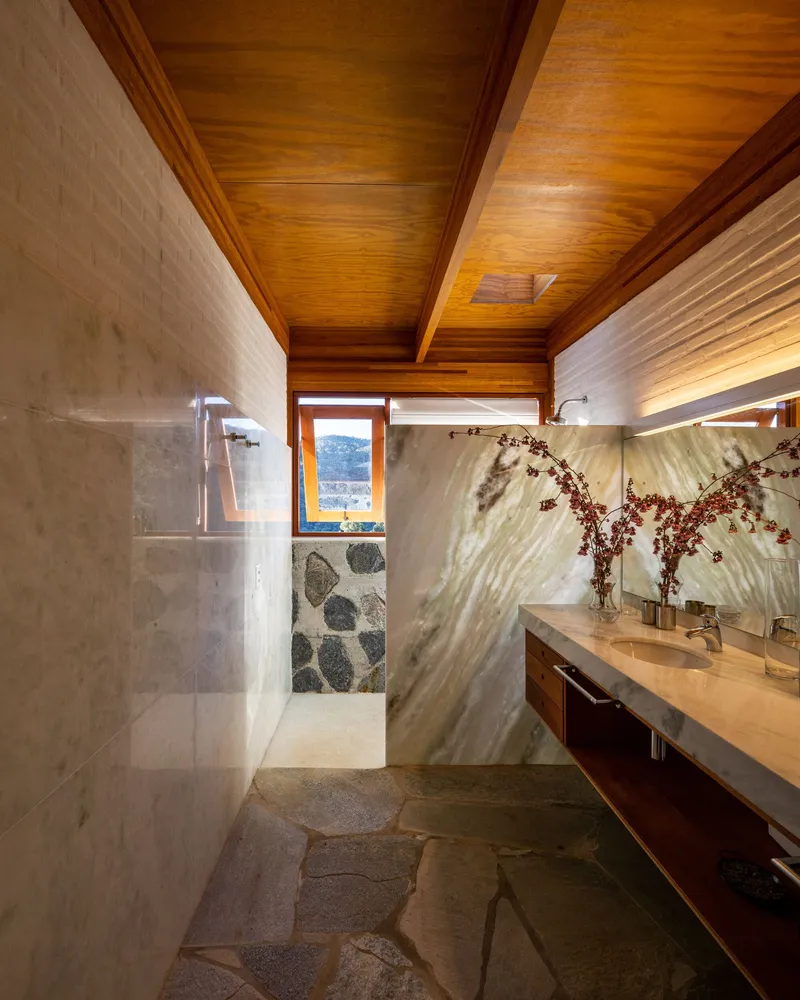 Bathroom with stone floor, veined marble wall panels, timber ceiling, and a window framing mountain views