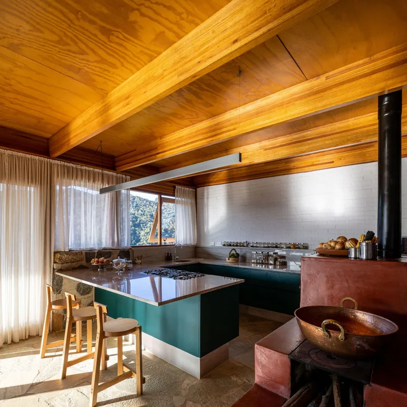 Kitchen with green island and wood-burning stove beneath exposed timber beams and a slatted wood ceiling