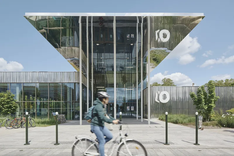 Glazed entrance with cantilevered soffit and cyclist passing on the paved plaza below