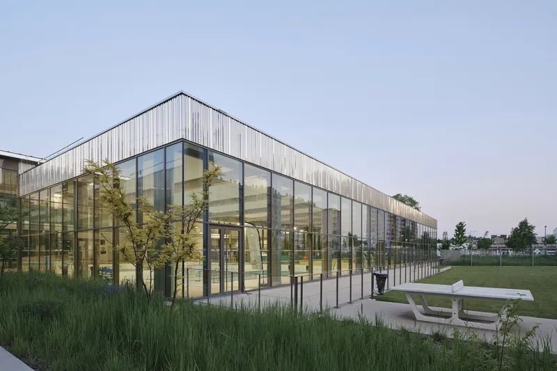 Corner view of the glazed facade and timber cladding at dusk with the adjacent lawn