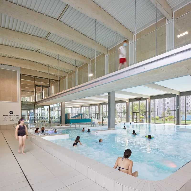 Indoor swimming pool with glass balustrade mezzanine, exposed timber beams, and bathers in the water