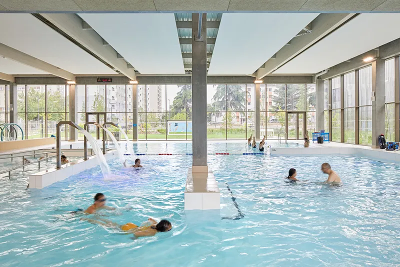 View across the pool to floor-to-ceiling glazing and a sunlit park beyond the water