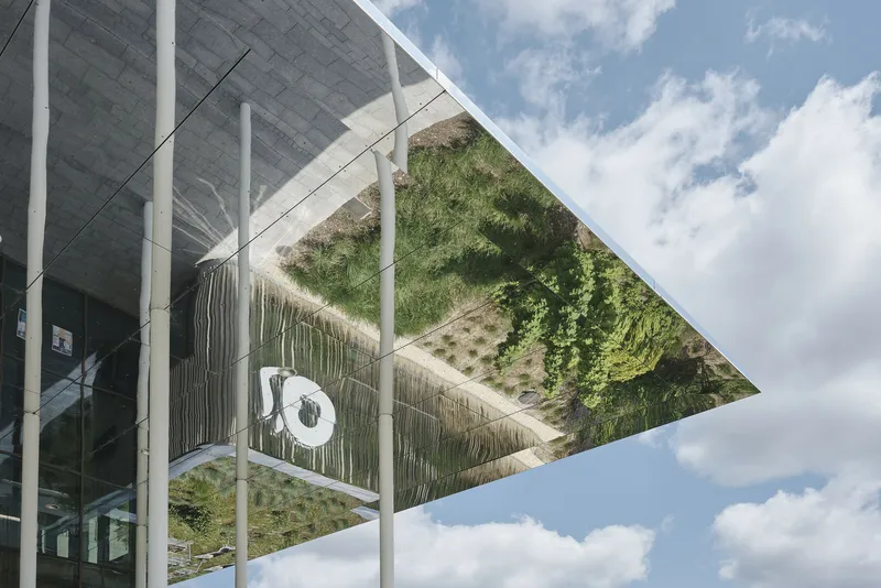 Upward view of the planted green roof framed by white structural columns against a cloudy sky