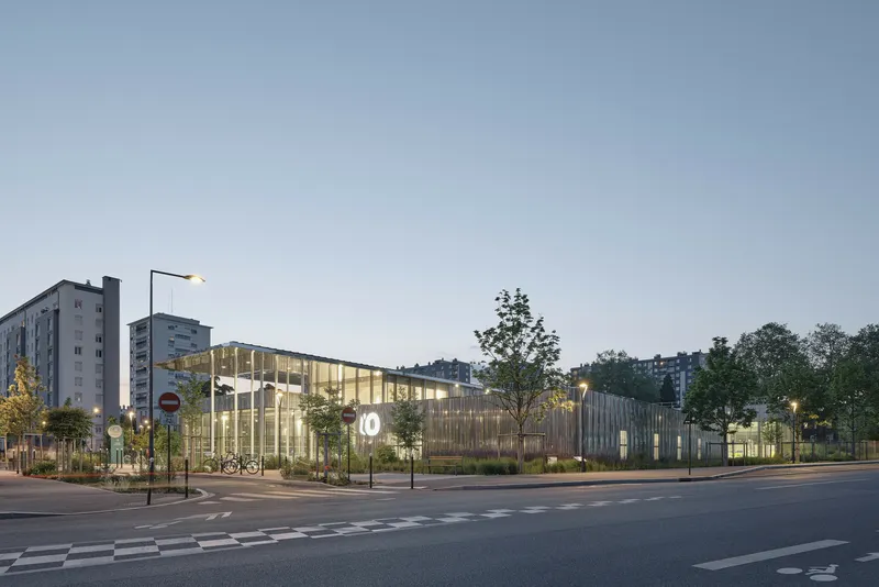 Street corner view of the illuminated glass facade with vertical timber screens at dusk