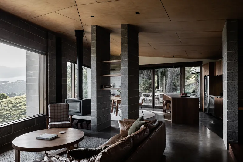 Open-plan living space with concrete block columns and plywood ceiling overlooking distant hills