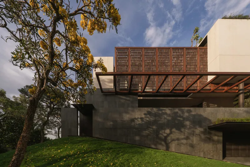 Concrete base with perforated terracotta screen balcony and yellow flowering tree in afternoon light