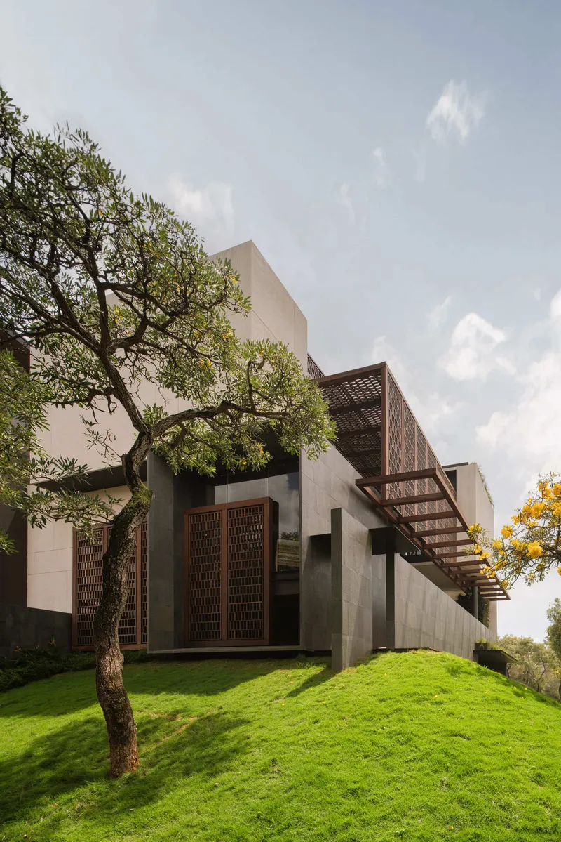 Facade showing terracotta lattice panels cantilevered over concrete volumes with trees framing the composition