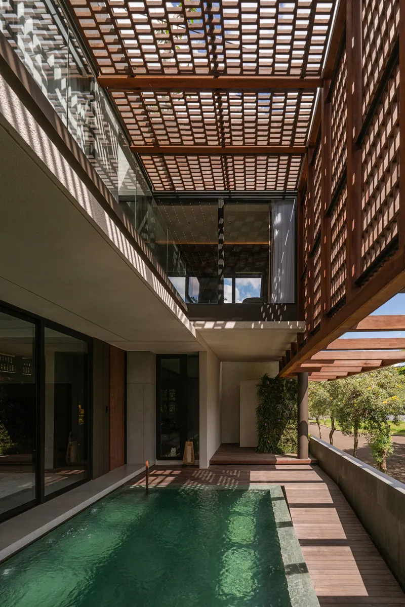 Courtyard pool with timber decking beneath layered terracotta screen pergola casting geometric shadows