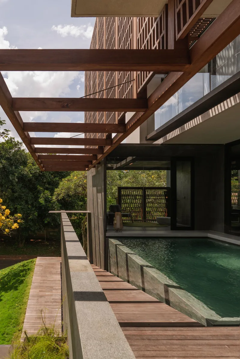 Pool deck with timber pergola beams extending toward sloped garden and yellow flowering trees