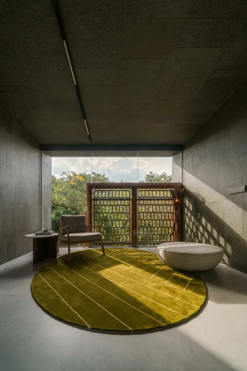 Concrete room with latticed timber screens framing the view and dappled sunlight on a green circular rug