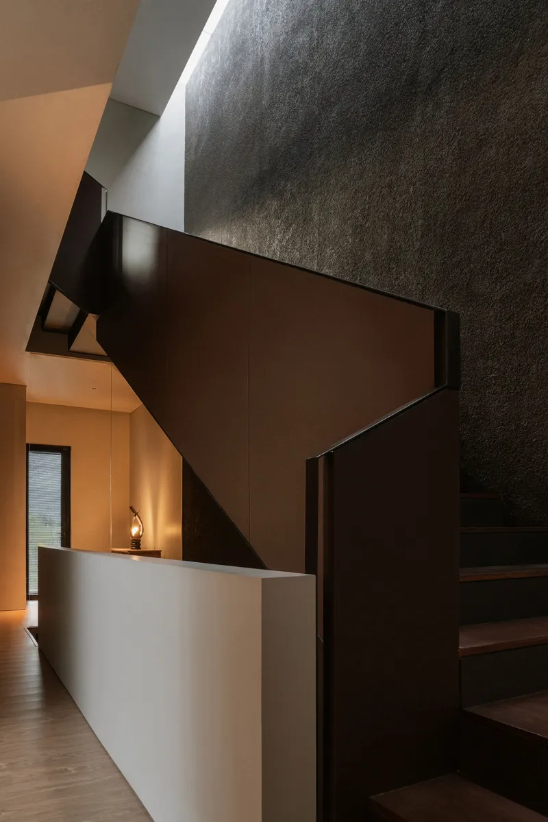 Dark timber staircase rising against textured concrete walls with warm light from below