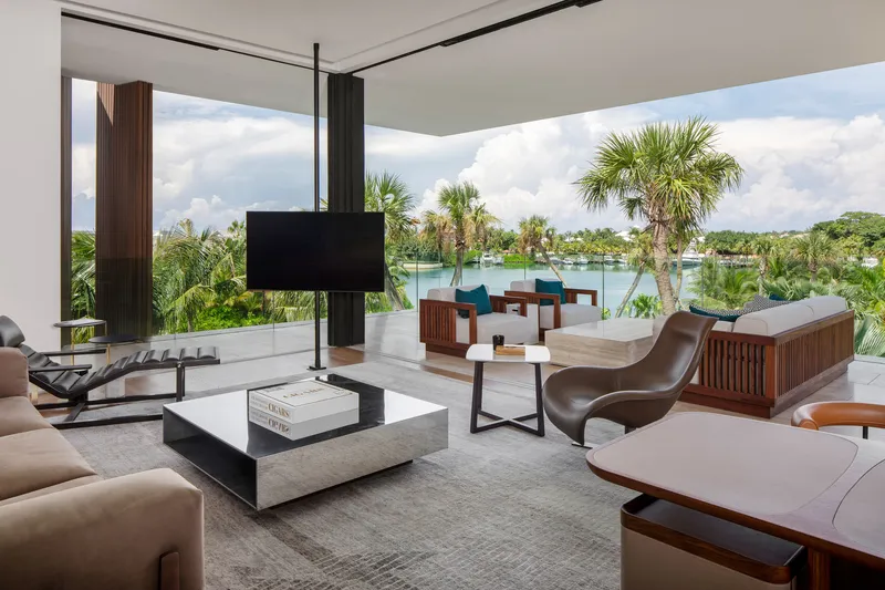 Open-plan living area with floor-to-ceiling glass walls overlooking lake and palm grove