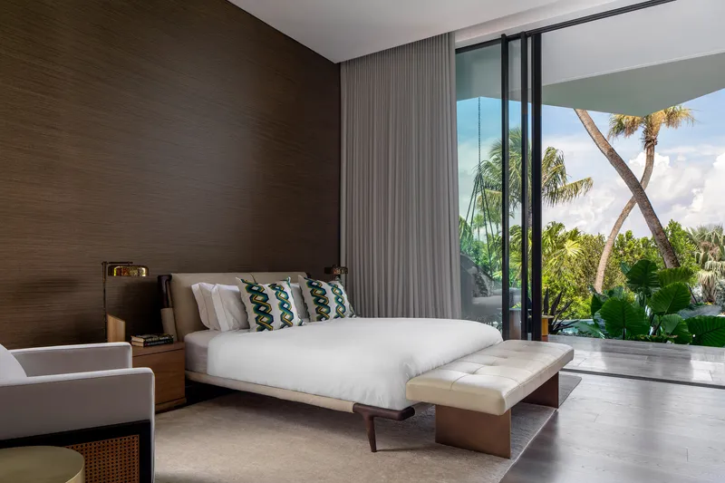 Bedroom with ribbed wood headboard wall and sliding glass doors to palm-shaded balcony