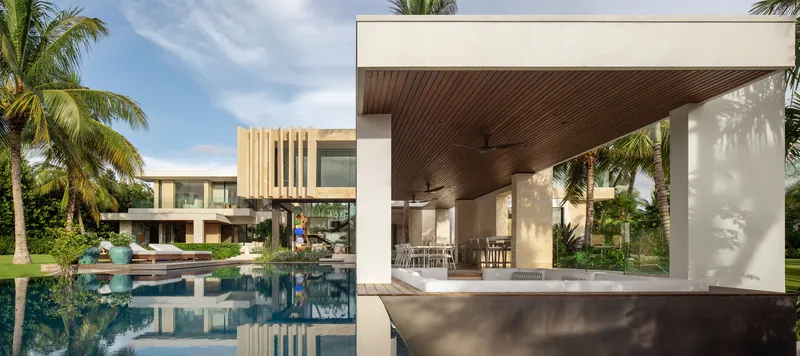 Poolside pavilion with timber-lined ceiling and white walls reflecting in still water at midday