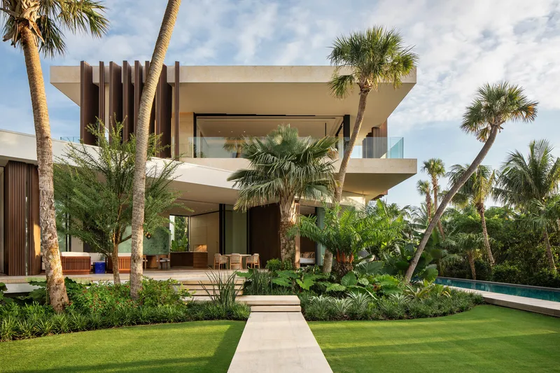 Garden view of the two-story residence with vertical timber screen and horizontal concrete balconies among palm trees