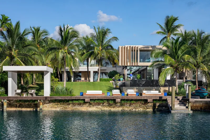 Waterfront facade seen from the dock with loungers and a freestanding pavilion framed by coconut palms
