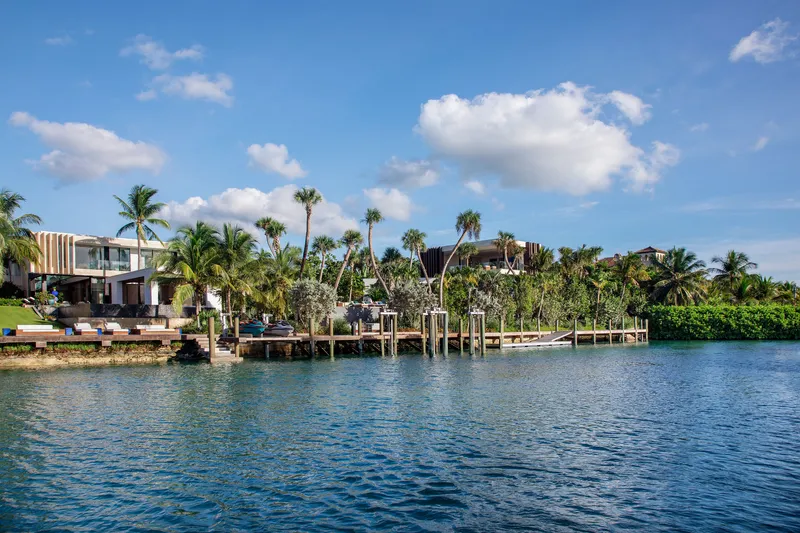 Waterside compound view with timber dock and multiple pavilions set among palms under scattered clouds