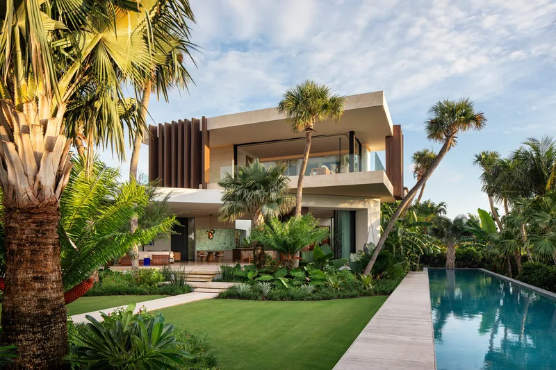 Two-story facade with vertical timber screen and glass balconies surrounded by palms and tropical planting