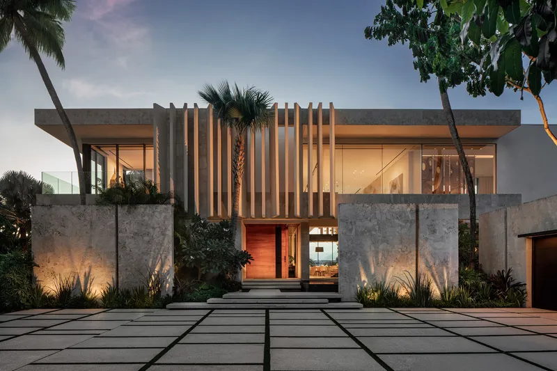 Entry facade with vertical timber louvres and stone walls illuminated at dusk beneath palm trees