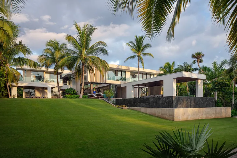 Rear elevation showing stacked volumes with timber screens and pavilions across sloping lawn at sunset