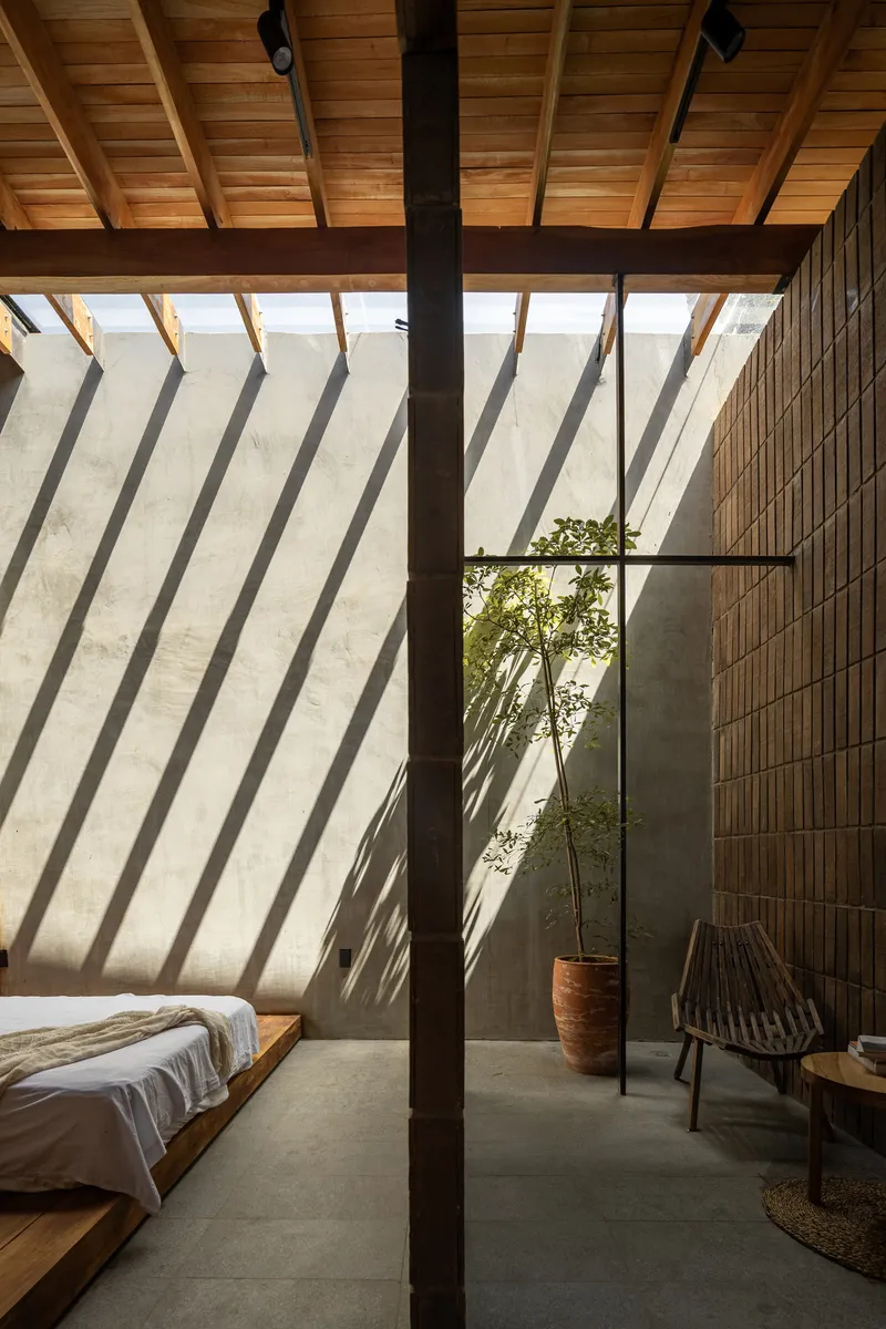 Bedroom with concrete walls and timber rafters framing slanted sunlight from a skylight above