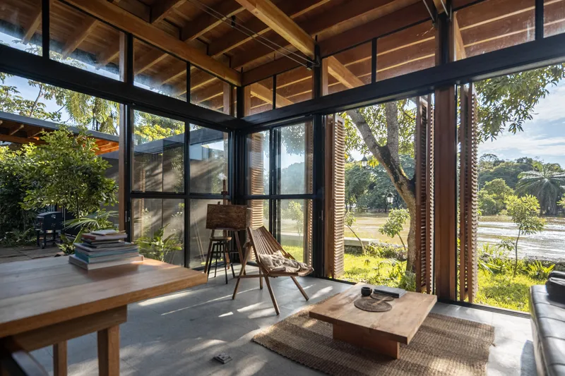 Corner seating area with floor-to-ceiling steel-framed glazing and timber louvered screens overlooking the garden