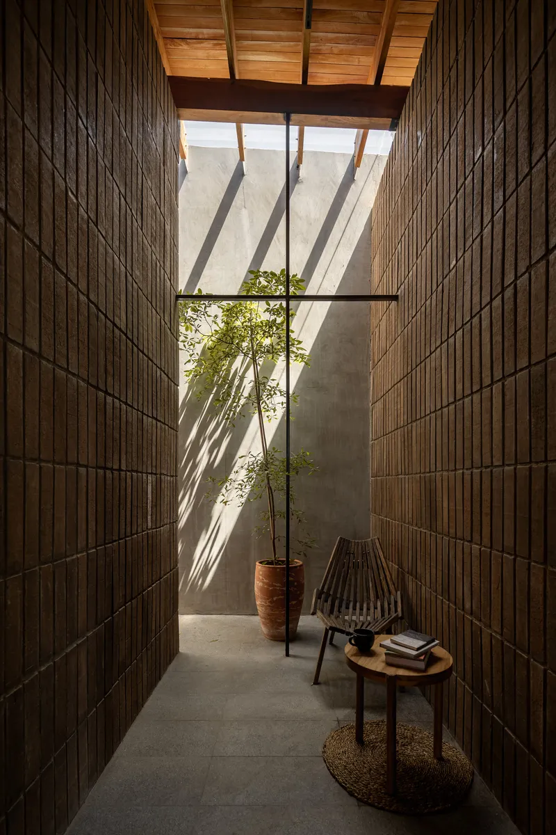 Narrow courtyard with vertical timber and brick walls, receiving angled shadows from overhead timber beams