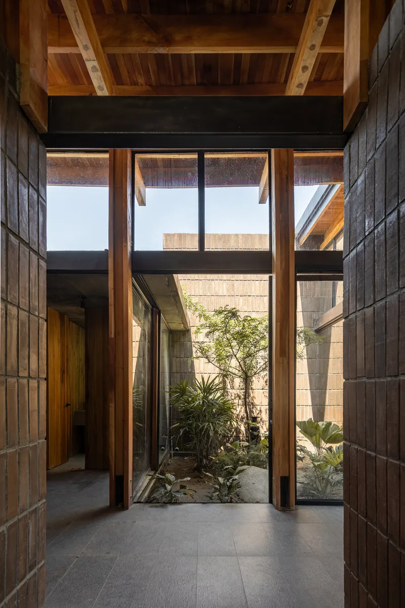 Entrance hallway with timber-framed glazing opening to a small planted courtyard with brick walls