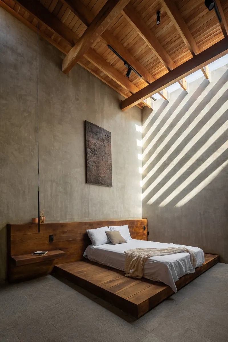 Bedroom with low timber platform bed beneath a vaulted wooden ceiling casting striped shadows