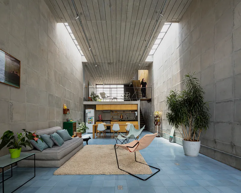 Double-height living space with concrete block walls, timber-slat ceiling and a steel mezzanine overlooking the dining area