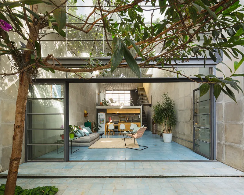 View from the planted courtyard through fully opened steel-framed glass doors into the double-height living space