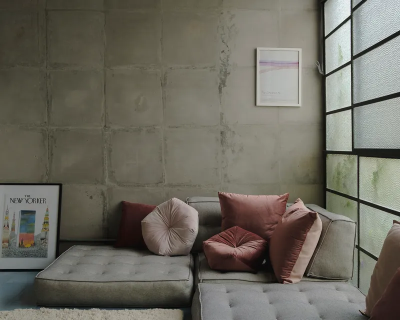 Corner seating area with board-formed concrete wall and translucent glass block window above grey sectional sofa