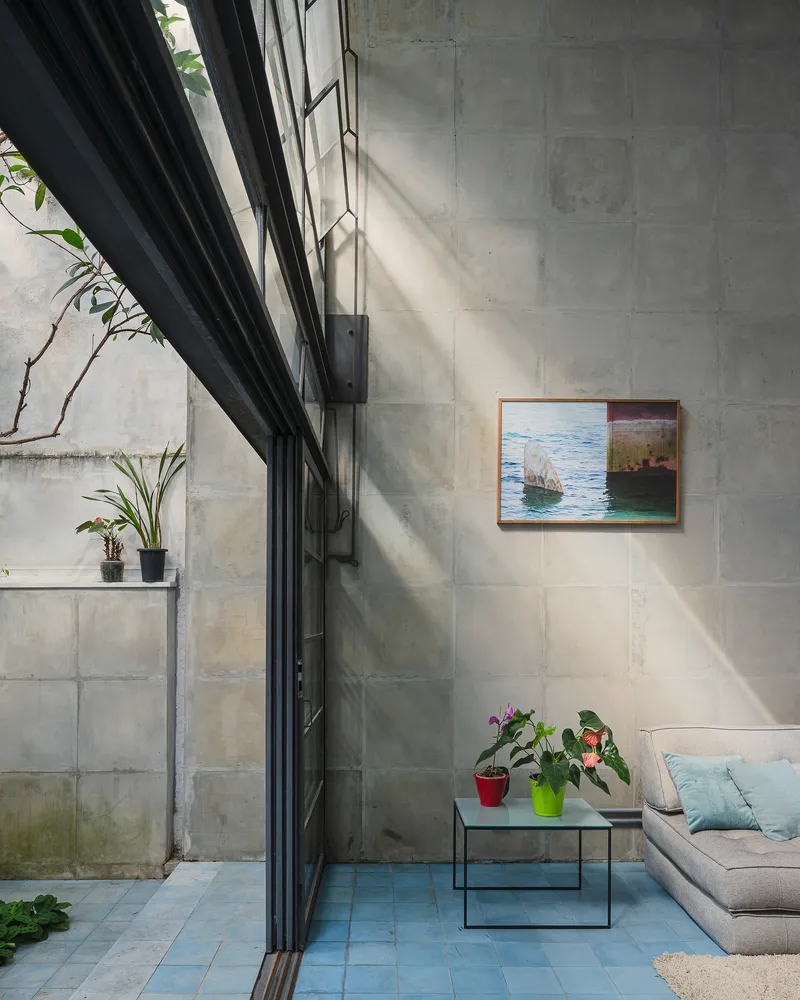 Double-height space with concrete block walls, black steel-framed glazing, and sunlight casting diagonal shadows