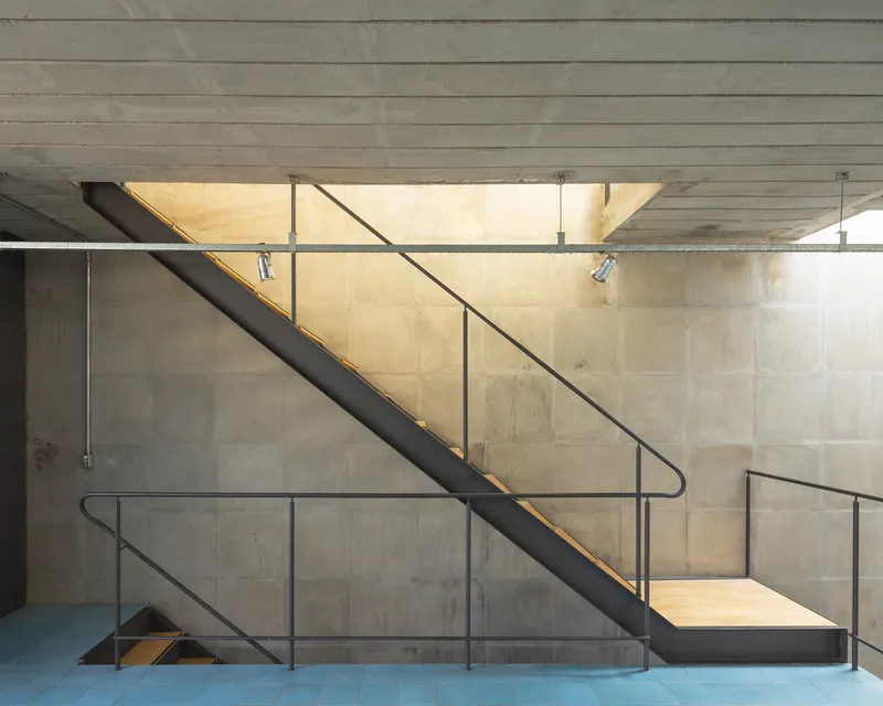 Steel staircase with tubular handrails and brass LED strip lighting against board-formed concrete walls
