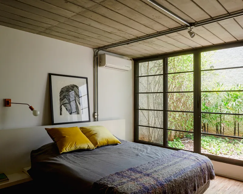 Bedroom with gridded steel window wall overlooking planted garden with bare branches