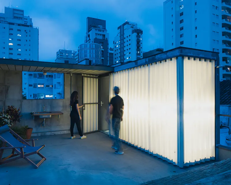 Rooftop terrace with backlit corrugated panel enclosure and two figures at dusk