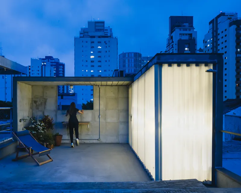 Rooftop terrace with translucent corrugated walls and glass pavilion at dusk with city skyline beyond