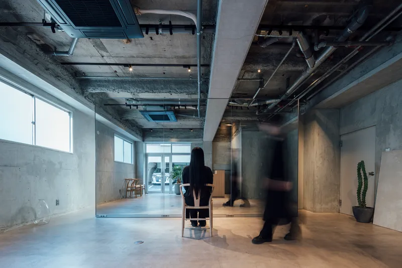 Long view through glass partitions with figure seated and another walking past in blur