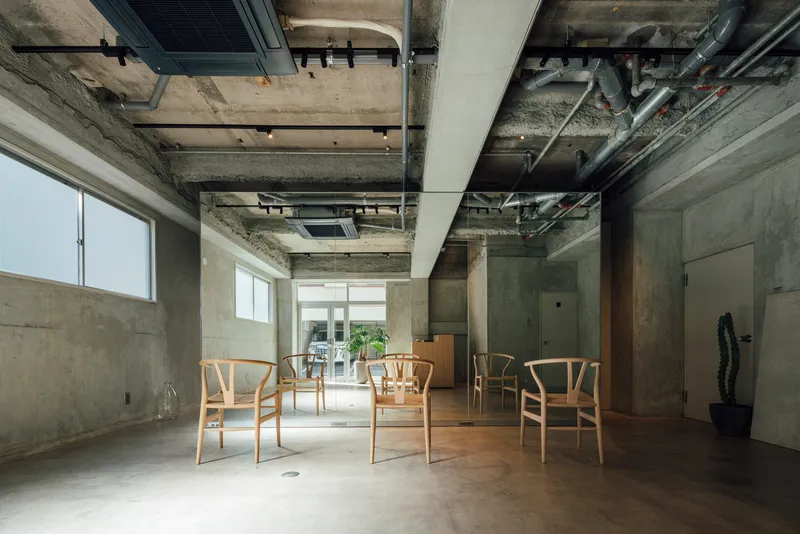 Interior with exposed concrete ceiling and mechanical systems above wooden chairs on polished floor