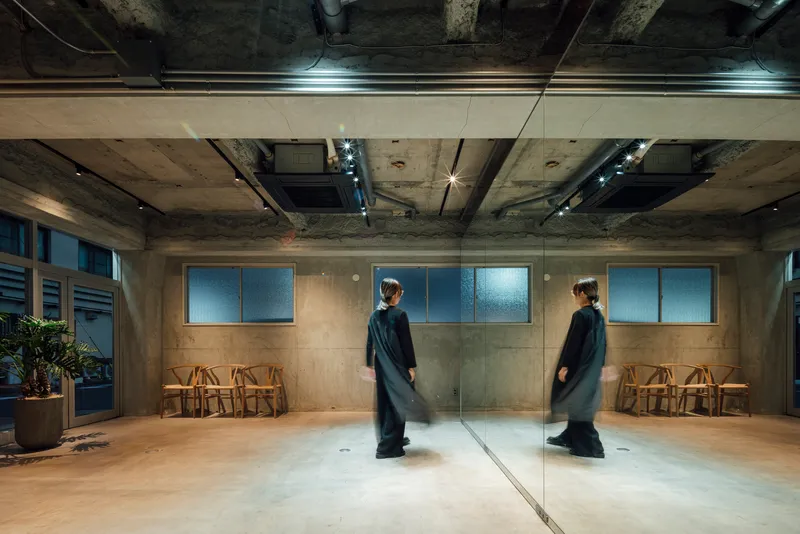 Interior space with exposed concrete ceiling and full-height mirror reflecting a figure in black