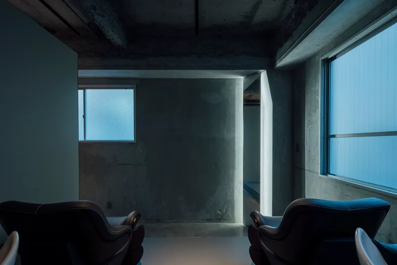 Concrete doorway framing a narrow passage with backlit translucent glazing between two salon chairs