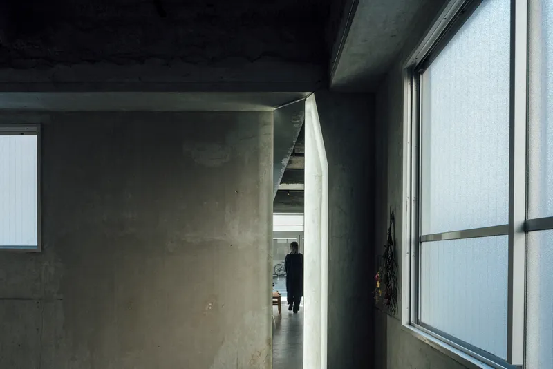 Concrete corridor with a figure visible through an angled doorway beneath a dark painted ceiling
