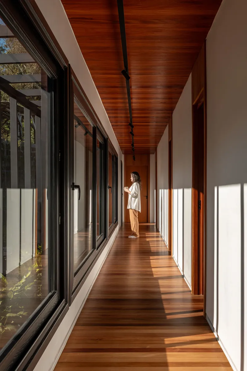 Timber-lined corridor with full-height glazing on one side casting afternoon light across the floor